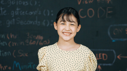 Cute happy girl smiling to camera while standing at blackboard with engineering prompt or coding,...
