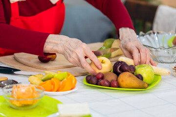 Close up of senior woman cutting fruits in the kitchen at home.