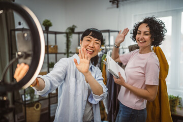 Naklejka premium Two diversity woman sell clothes live stream on mobile phone at home