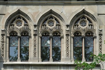 Fototapeta premium Close-up of three arched windows with intricate stonework and keystones on a stone building, Arched windows with ornamental keystones and intricate trim