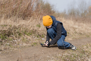 A child takes pictures on a phone with an additional macro lens for phones on the ground of bugs, ants. The concept of children's curiosity, gadgets. exploring the world around him