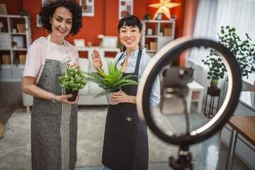 Two multicultural woman use cellphone for live stream about home plant