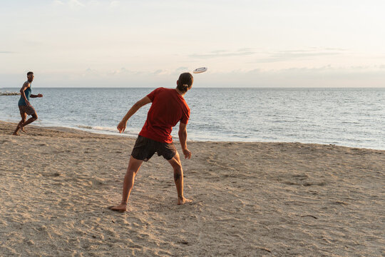 Two men playing frisbee on a beach at sunset