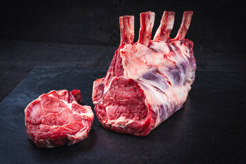 Raw dry aged bone-in back rack of veal loin offered as close-up on a black board