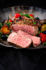 Traditional barbecue dry aged veal chop Mediterranean vegetable and fried potatoes served as close-up in a rustic cast iron frying pan on a wooden table