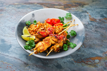Authentic Sate Ayam - grilled chicken satay sate skewers with stir-fried rice and vegetable served as close-up on a design plate