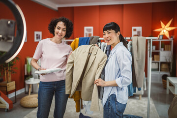Fototapeta premium Two diversity woman sell clothes live stream on mobile phone at home