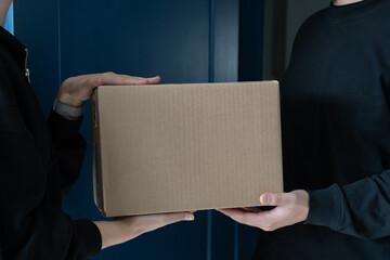 close-up customer receiving a cardboard box parcel at the door from delivery person. Courier is...