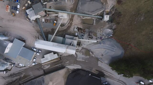 Aerial view of an active mining site in the Alps, showing machinery, vehicles, conveyor belts, and piles of materials amidst a mountainous landscape.