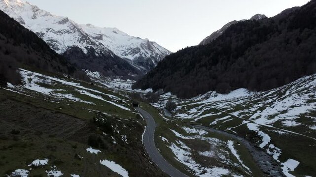 Aerial shot - Mountain landscape revealing snow covered peaks, winding road traversing rugged terrain in Pyrenees National Park spanning Franco Spanish border