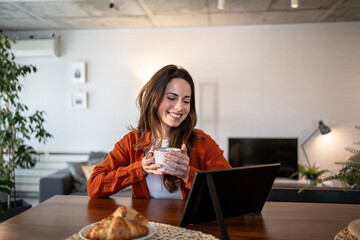 Happy woman having breakfast and video calling with tablet at home