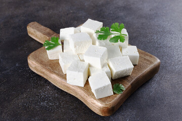 Cubes of Indian paneer cheese on a wooden board on a gray background. Indian food.