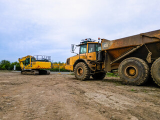 Heavy-duty articulated dump truck and tracked excavator parked on a dirt construction site, captured under an overcast sky, ready for earthmoving and groundwork operations