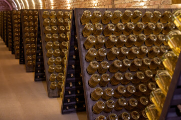 Bottles on racks in deep and long undergrounds caves, making champagne sparkling wine from chardonnay and pinor noir grapes in Reims, Champagne, France
