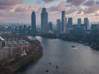 Aerial perspective of London featuring the River Thames, modern high rise buildings, active boats, and tree lined streets with residential areas.