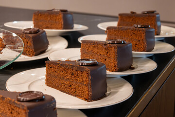 Many white plates with pieces of famous Sachertorte chocolate cake with apricot jam of Austrian origin in kitchen of old classic cafe-restaurant in Vienna