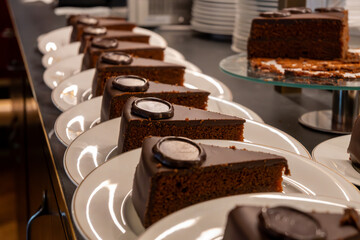 Many white plates with pieces of famous Sachertorte chocolate cake with apricot jam of Austrian origin in kitchen of old classic cafe-restaurant in Vienna