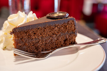 Piece of famous Sachertorte chocolate cake with apricot jam of Austrian origin served with whipped cream in old classic cafe-restaurant in Vienna