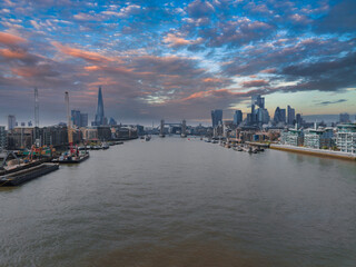 Fototapeta premium Aerial view of London with the River Thames, Tower Bridge, the Shard, City of London skyscrapers, riverside developments, and a cloudy sky.