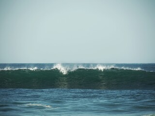 A wave breaks on the beach on a sunny day.