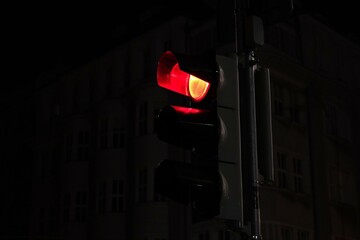 Red traffic light glowing in darkness at night, city background out of focus