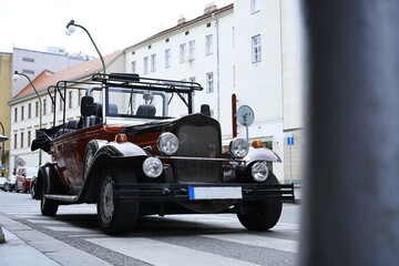Vintage red convertible car with open roof parked on a narrow Prague street.