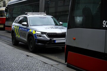 Czech police SUV standing between red trams on a cobblestone street © VladyslavShcherbakov