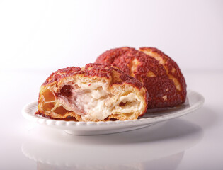 choux pastry with vanilla cream and cherry on white plate, on white glass background, copy space, close up