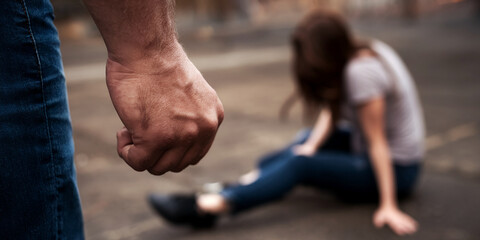 Close-up of clenched fist, blurred woman in background, depicting violence, aggression, and abuse.  Symbolizes threat and vulnerability