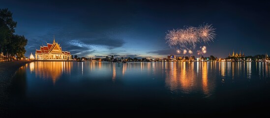 Obraz premium A panoramic view of a temple reflecting in a calm lake at night with fireworks in the distance.