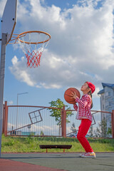 A child on a kindergarten playground aims a basketball at a basketball hoop