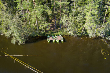Aerial shot: Four green canoes moored at a wooden dock on a forest river or lake shore.