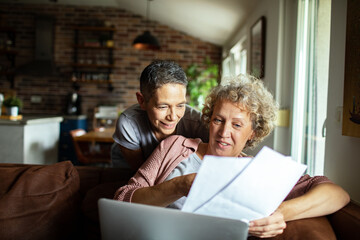 Senior lesbian couple using laptop on cozy couch at home