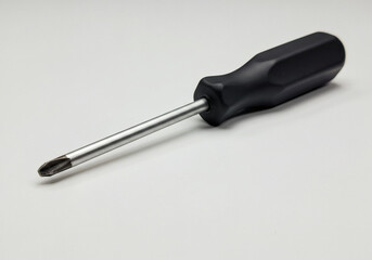 Black screwdriver with ergonomic handle and metal shaft featuring Phillips head tip, professional hand tool for fastening and unfastening screws against clean white background.
