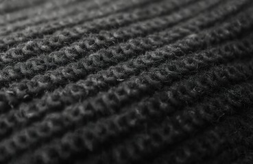 Black knitted wool textile material background. Dark grey cotton fabric woven canvas texture. Warm clothing design, winter fashion, detail, closeup macro.