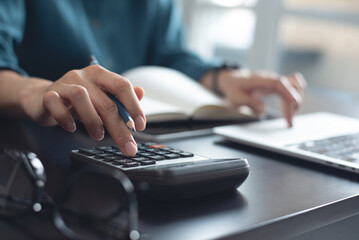 Close up, business woman working at office, using calculator to calculate company finance, accounting with laptop computer on table, budget management. Doing finance, budgeting and tax calculation