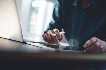 Business woman using digital tablet and working on laptop computer on table at office. Close up. Woman surfing the internet, using tablet pc searching the information, online working from home office