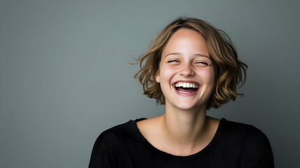 Joyful Portrait Of A Young Woman With Blonde Hair Laughing With Wide Smile Against Gray Background