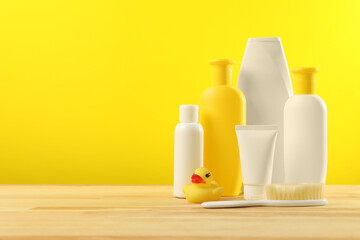 Baby cosmetic products and bath accessories on wooden table against yellow background. Space for text