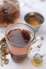 Delicious herbal tea with honey and dry leaves on white marble table, closeup