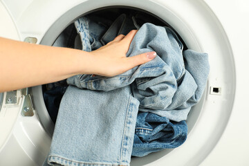 Woman putting jeans into washing machine, closeup