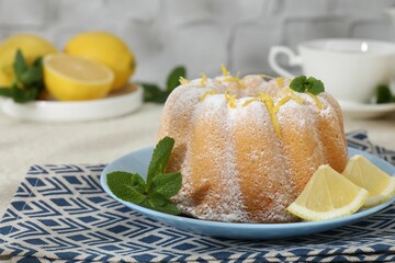 Delicious cake with lemon zest, powdered sugar and mint on light textured table, closeup