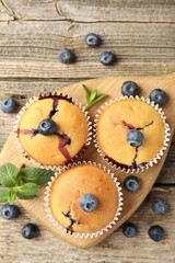 Delicious muffins with blueberries and mint on wooden table, flat lay