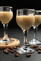 Coffee cream liqueur in glasses and beans on black table, closeup
