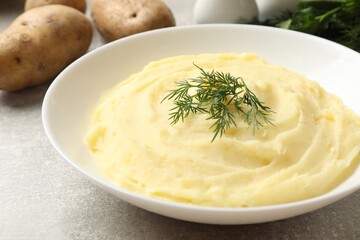 Tasty mashed potato with dill in bowl and raw vegetables on grey textured table, closeup