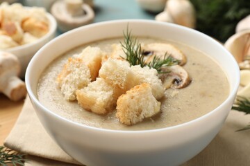 Delicious mushroom cream soup with croutons and dill on table, closeup