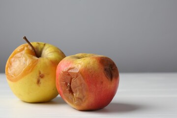 Rotten apples on white wooden table against grey background, closeup