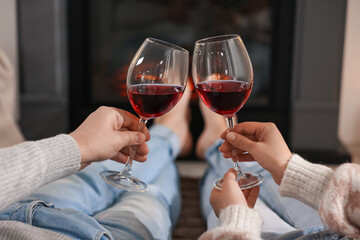Couple with glasses of wine near fireplace on floor at home, selective focus