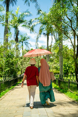 Couple walking in the park under an umbrella on a sunny day