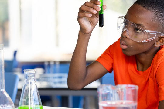 In school, boy examining test tube in science classroom, wearing safety goggles
